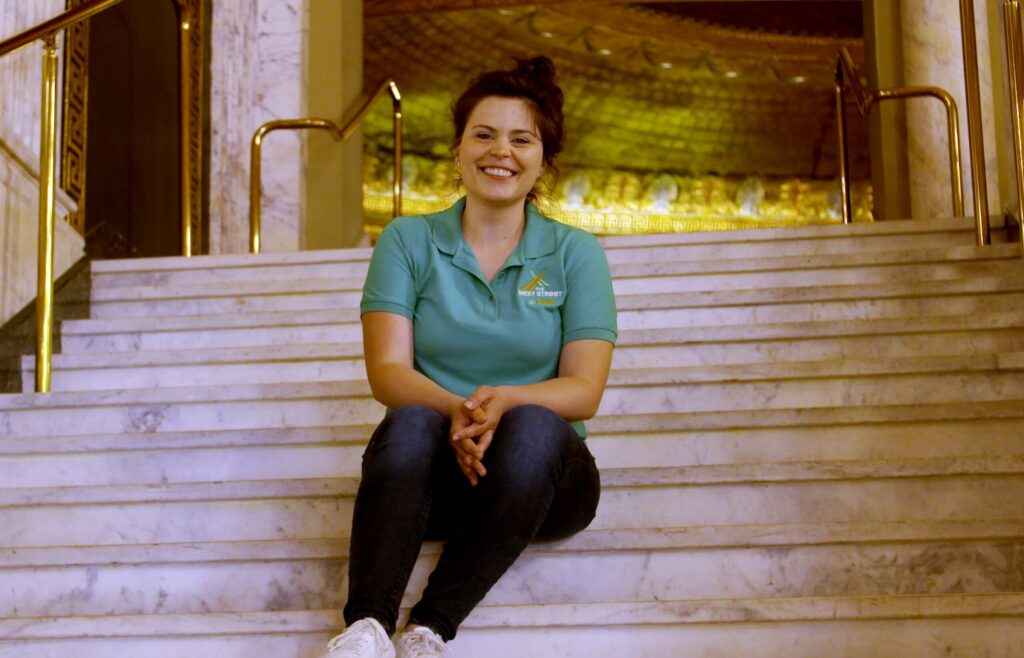 Image description: a photo depicts Mandy sitting on steps, wearing her next street uniform and a warm smile.